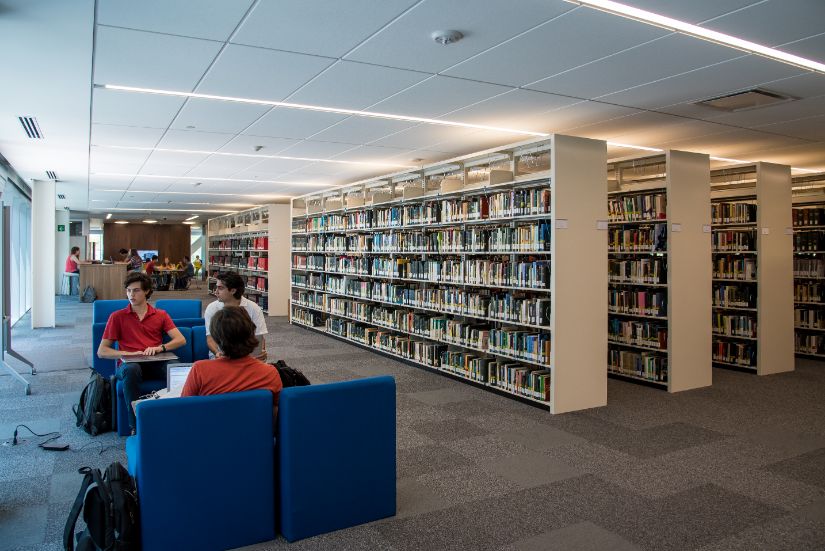 Pasillos de libreros en Bibliotec, con alumnos sentados cerca
